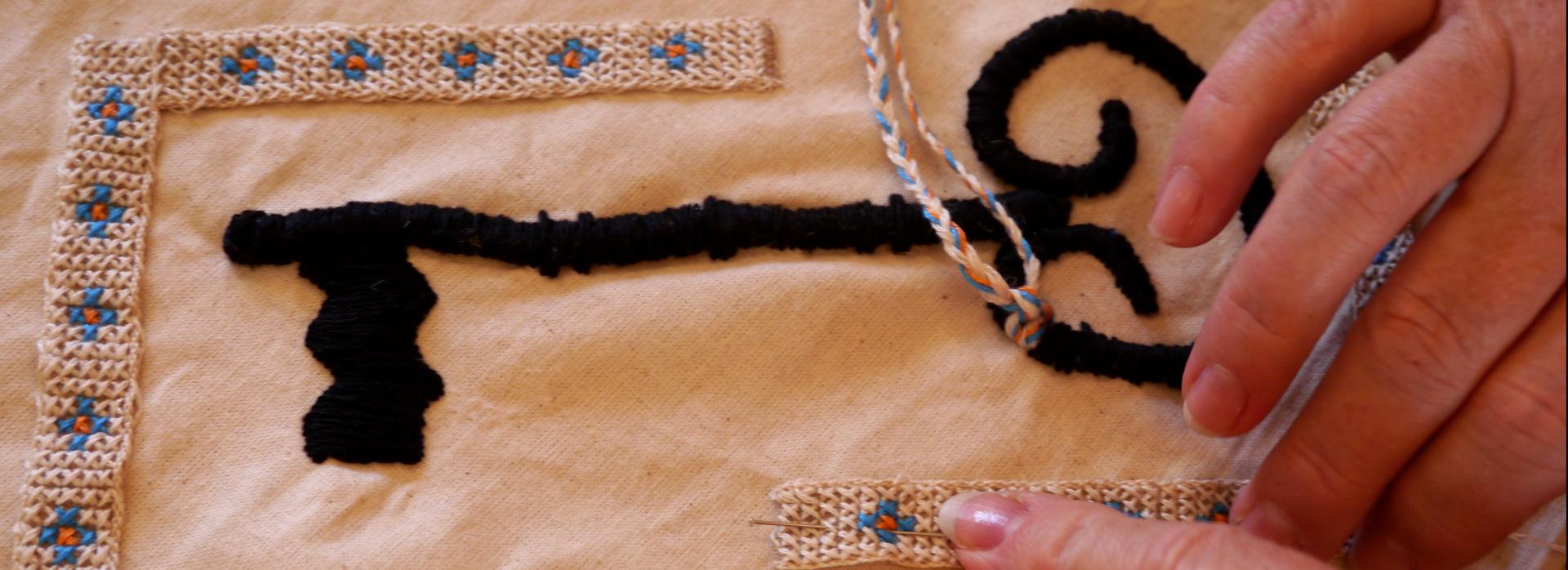 a close-up of two hands working on an embroidery of a key
