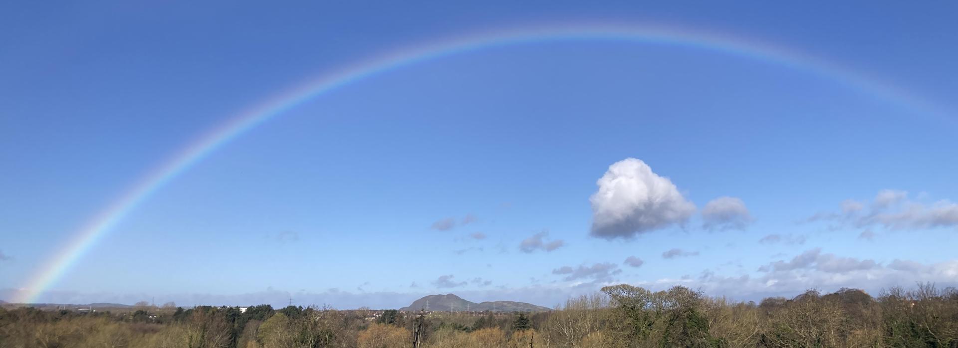 photo of a rainbow in a blue sky with a single cloud underneath it