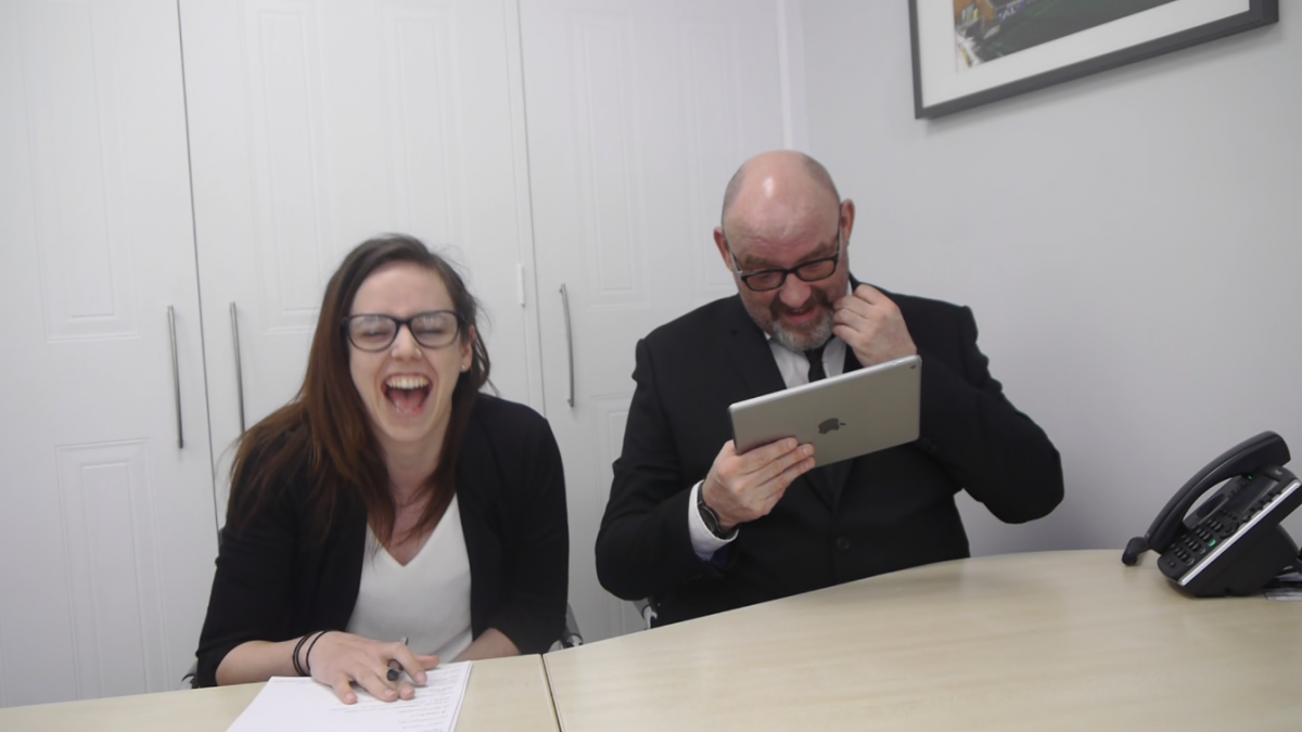 Kelly and a colleague sit at a table, Kelly is laughing