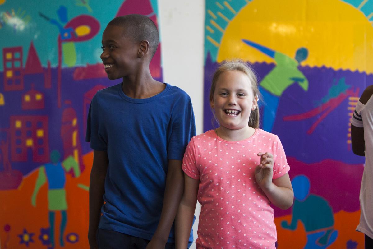 two young carers standing and smilling in front of a colourful artwork in the background