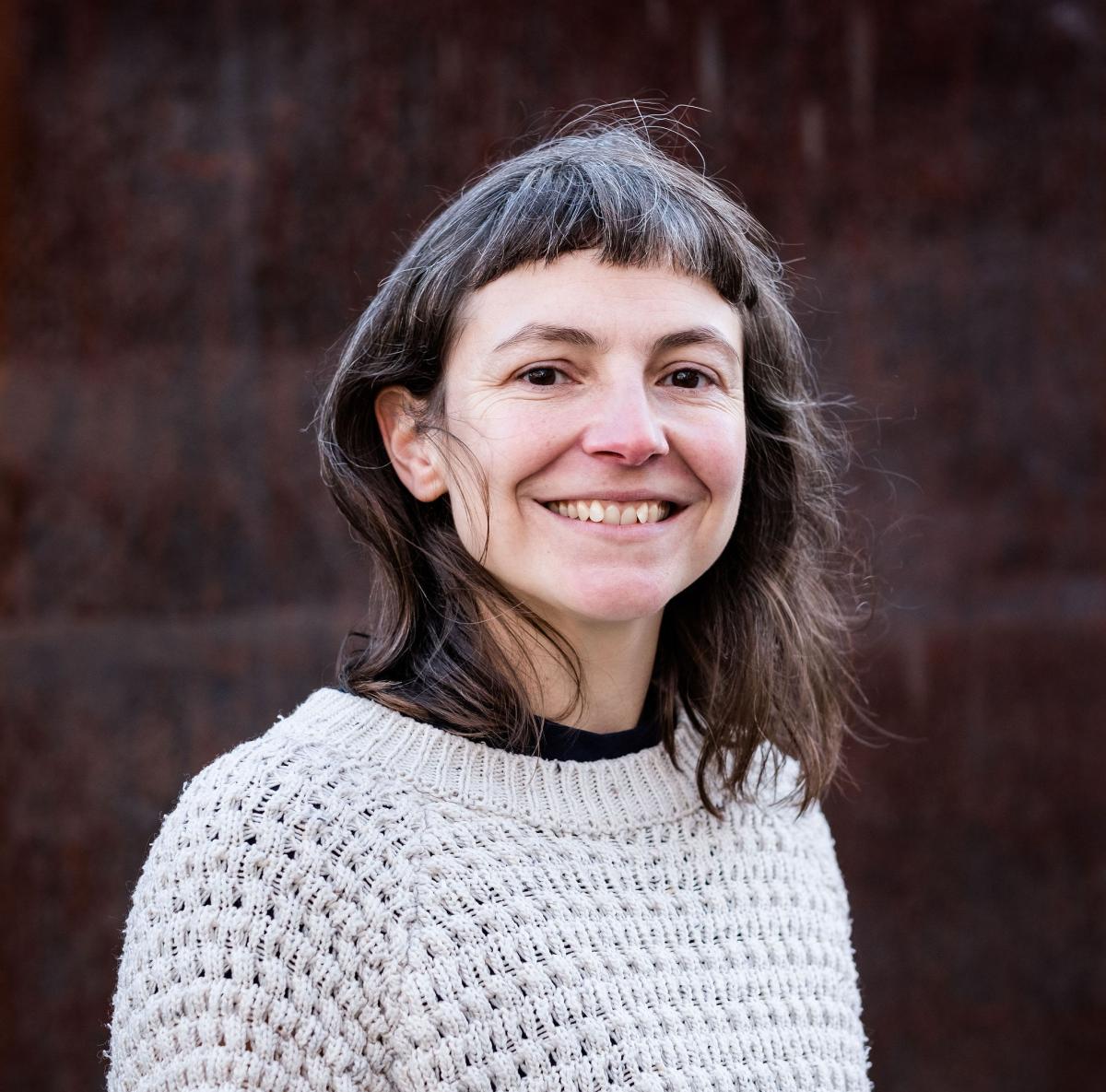 a half-length photo portrait of a woman with dark hair wearing a pale grey sweater