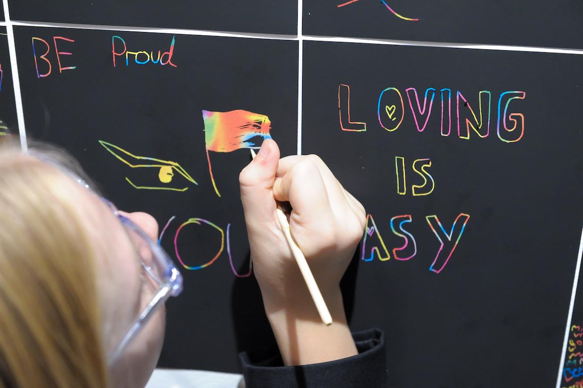 A person colours in a rainbow flag on a board