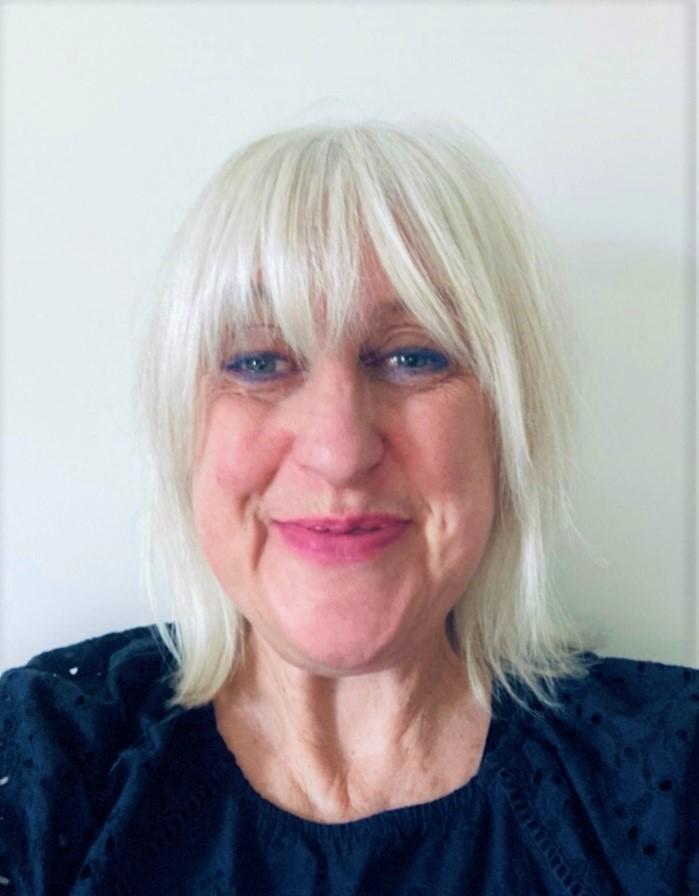 Close up photograph of middle aged white woman with shoulder length white hair wearing a navy blue round neck top