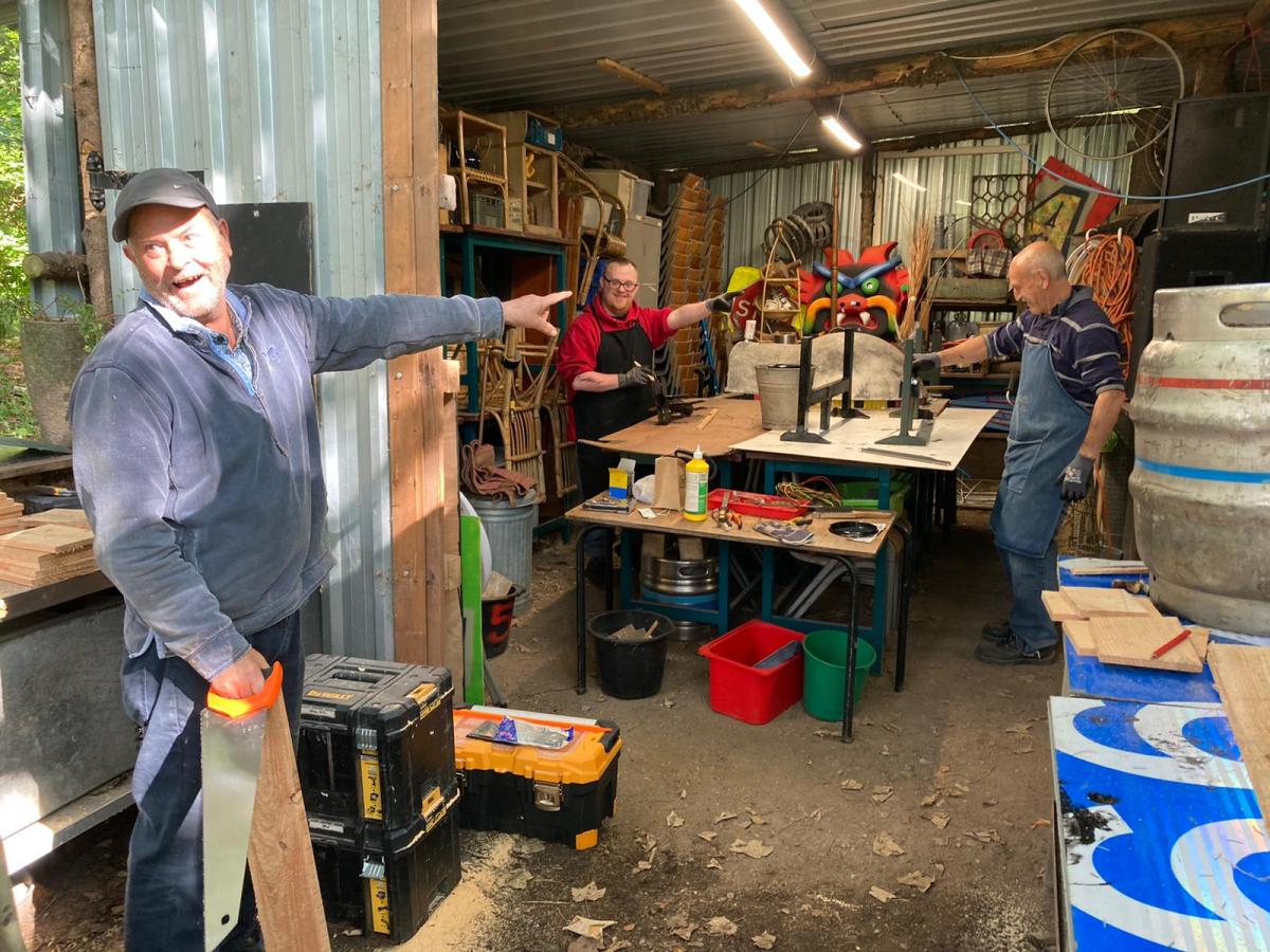 a laughing man points into a shed where two other men are working