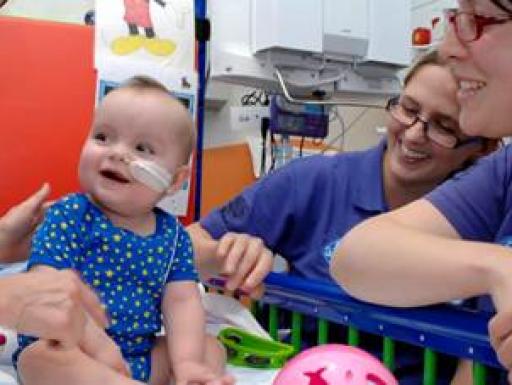 Nurses surround a baby in hospital, smiling