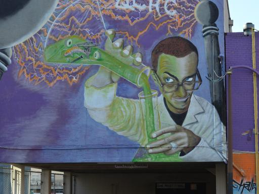 wall graffiti image of a man in a lab coat pouring green chemicals into a glass vessel