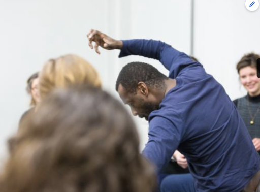 A black man in a blue top leaning to the side with his arm over his head