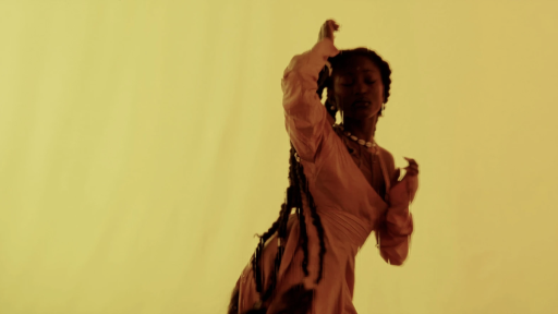 a black woman with long braids dancing against a yellow background