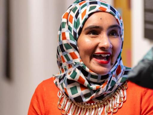 close-up photo of a woman in a colourful headscarf and orange top speaking animatedly in a group setting