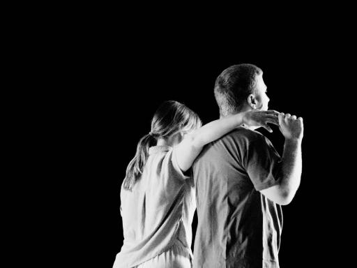 Two dancers with their backs to camera, one with their arm around the other